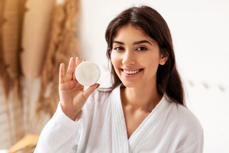 Pretty Female Showing Moisturizer Cream Jar To Camera In Bathroomの写真素材