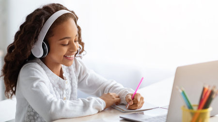 Cheerful school girl having online lesson, using laptop at homeの写真素材