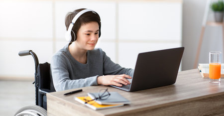 Disabled teen boy listening to music while doing online homework on laptop, indoorsの写真素材