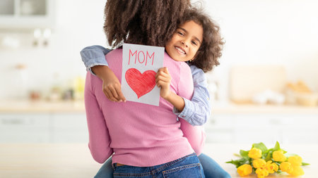 Happy black daughter greeting mom with tulips and cardの写真素材