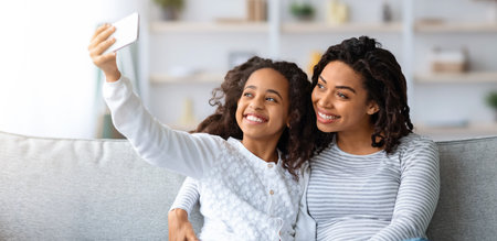 Beautiful black mother and daughter taking selfie on smartphoneの写真素材
