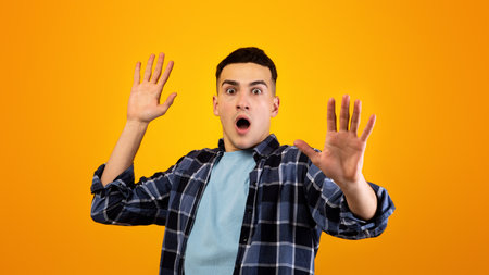 Scared Caucasian guy shouting in panic, making STOP gesture with both hands over orange studio...