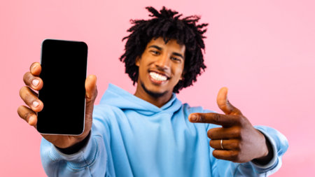 Happy black teen guy pointing at smartphone with mockup for website or app design on blank screen...