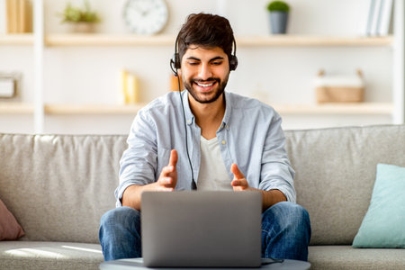 Video conference concept. Arab man in headset having web call on laptop, working remotely from home
