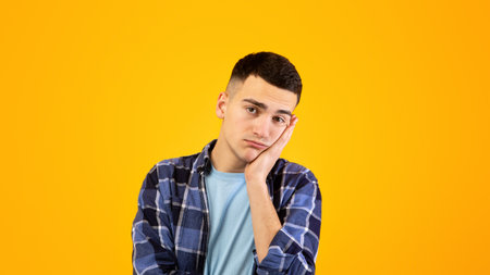 Portrait of young guy feeling bored, leaning on his hand, having dull day on orange studio...