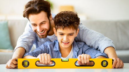 Happy father teach son using level tool for measure surface, doing apartment repair together...