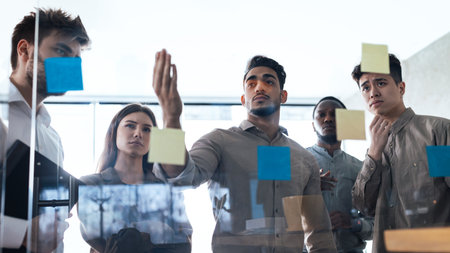 Colleagues having meeting using sticky post-it notes on glass wall