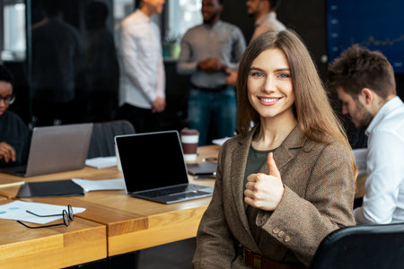 Confident businesswoman sitting at desk showing thumbs up gesture