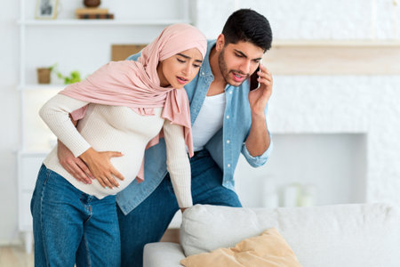 Worried arab husband calling doctor or ambulance while his pregnant wife having prenatal contractions, copy spaceの写真素材