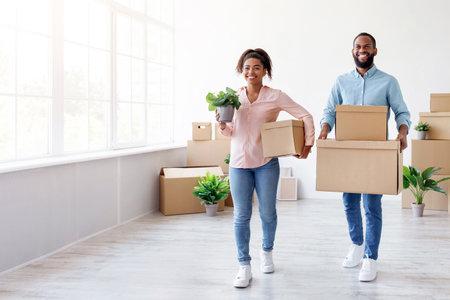 Satisfied happy millennial african american male and female carry cardboard boxes with belongings in...
