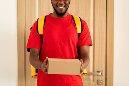 Black delivery man holding box standing at door