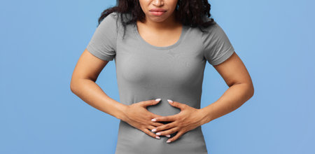 Black woman touching aching abdomen having painful stomachache standing over blue studio background