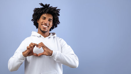 Kind black teenager shaping hands like heart near his chest, making love gesture on violet studio backgroundの写真素材