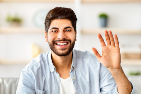 Greeting gesture concept. Happy arab man waving hand to camera, saying hello and laughing