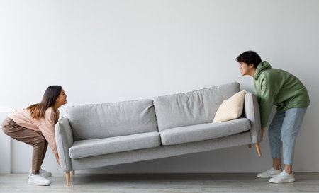 Happy young Asian couple moving sofa in living room, replacing furniture at home, copy spaceの写真素材
