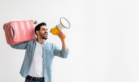 Young arab tourist man with luggage suitcase on shoulder screaming on megaphone and advertising tour agency offerの写真素材