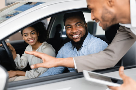 Joyful Couple Buying Car Talking With Salesman In Dealership Store