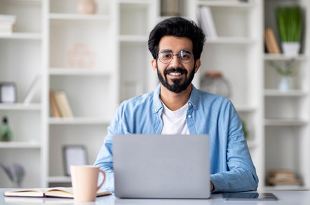 Handsome Young Indian Man Sitting At Desk With Laptop At Home