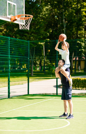 Happy father helps his son to score a basket outside