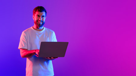Young caucasian guy using laptop in studio with neon light