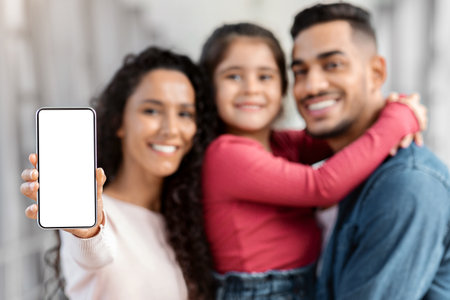 Happy Arab Family Showing Smartphone With Blank Screen While Standing In Airport
