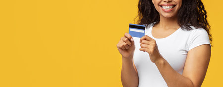 Easy digital cashless payment. Happy black woman holding credit card and smiling to camera, yellow...