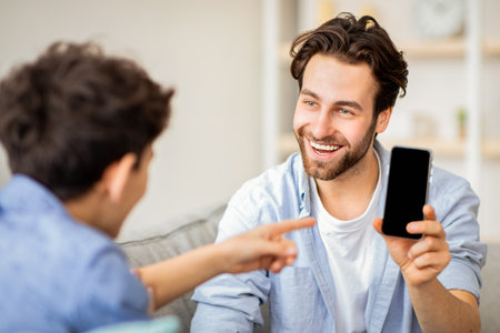 Handsome father showing smartphone with blank black screen to his son, place for mockup