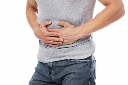 Cropped millennial european male suffering from abdominal pain and pressing his hands to sore spot