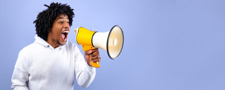 Cool news. Agitated African American teen guy screaming into megaphone over blue studio background