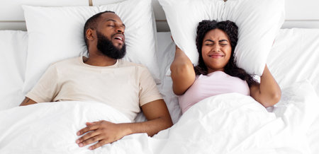 Angry upset young african american wife covers ears with pillow and suffers from husband noise