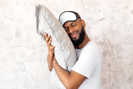 Smiling bearded afro guy hugging pillow at home