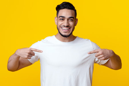 Excited arab guy pointing at his blank white t-shirt