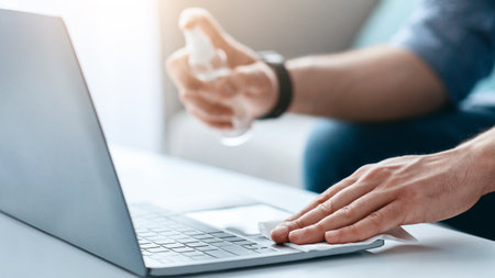 Device disinfection. Male hand using disinfectant spray and cloth for cleaning laptop keyboard