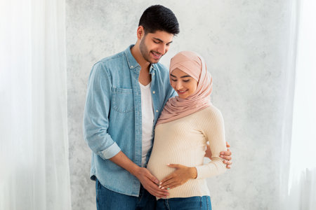 Parenthood concept. Loving arab pregnant woman and her husband embracing, smiling and touching belly
