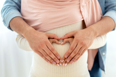 Closeup view of muslim pregnant woman and her husband hugging tummy together, making heart with...