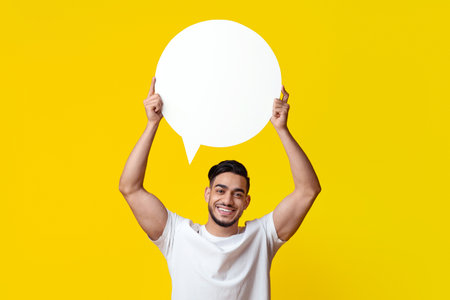 Middle eastern man holding blank speech bubble on yellow