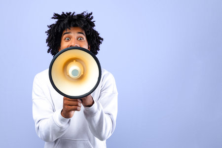 Emotional black teenager making announcement with megaphone on blue studio backgroundの写真素材