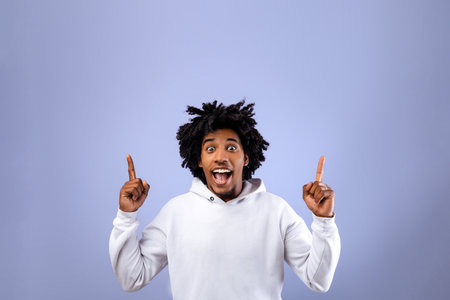 Cool black teenager pointing upwards with both hands on violet studio background, space for your ad...