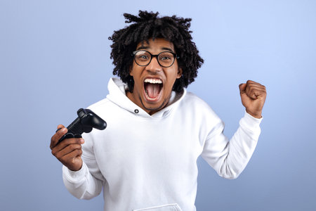 Triumphant teen guy with joystick shouting in excitement, playing video game, making YES gesture