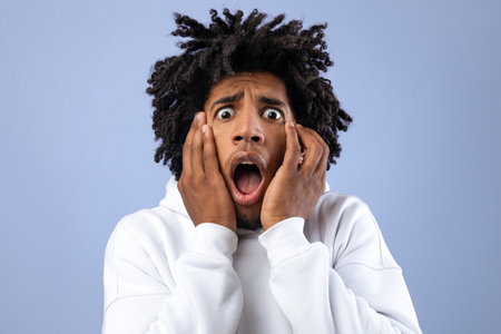 Black teen guy feeling scared, shouting in panic on violet studio background