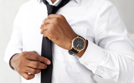 Man Adjusting Tie While Wearing Stylish Watch in a Well-Lit Indoor Setting
