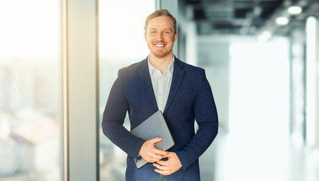 Handsome cheerful businessman posing with laptop at office