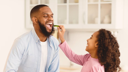 Cheerful african daughter cooking fresh salad feeding fatherの写真素材