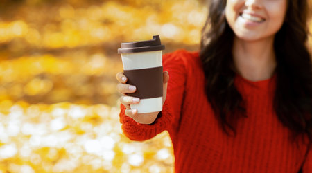 Lovely young lady in warm woolen sweater drinking fresh hot coffee at autumn park, selective focus....