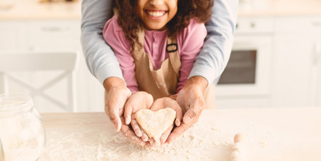 Happy black man and girl holding dough in heart shape