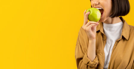 Healthy lifestyle concept. Young woman eating tasty apple on yellow background, biting fresh...