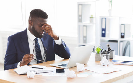 Tired afro businessman taking his glasses off, touching nose bridgeの写真素材