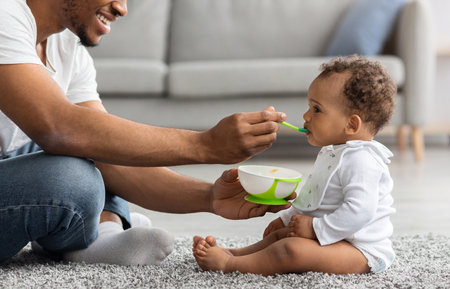 African American Father Feeding His Adorable Infant Baby Son With Spoonの写真素材