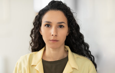 Portrait of focused young Latin woman in casual clothes looking at camera at homeの写真素材