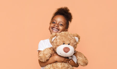 Little Girl Holding Teddy Bear and Smiling Against Peach Backgroundの写真素材